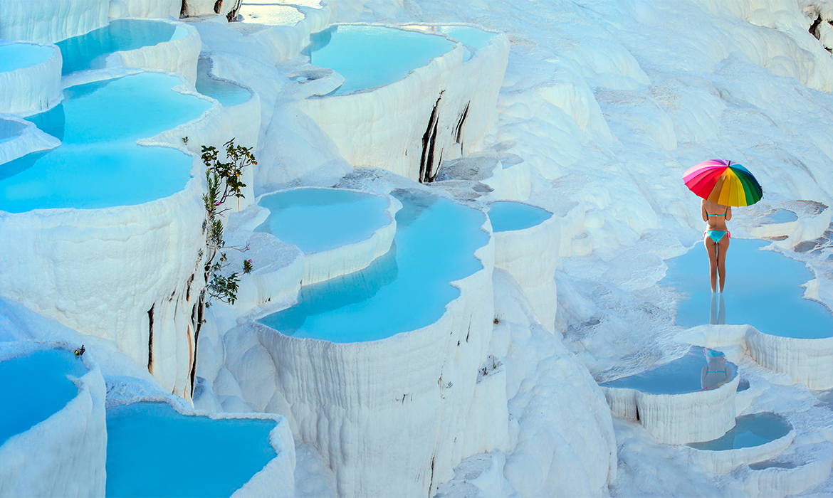 degraus de piscina natural. Agua de tom turquesa e rochas brancas. Modelo de biquini azul segurando um guarda chuva colorido em Pamukkale na Turquia